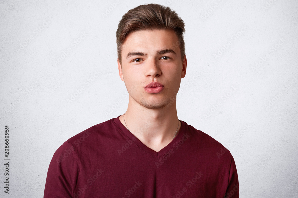 Portrait of handsome serious male teenager has trendy haircut, healthy skin, pouts lips and looks with confident expression, wears casual t shirt, poses against white background. People and youth Portrait of handsome serious male teenager has trendy haircut, healthy skin, pouts lips and looks with confident expression, wears casual t shirt, poses against white background. People and youth