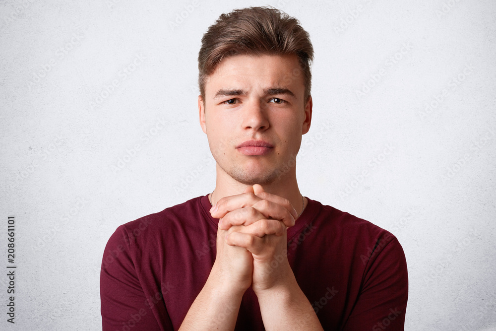 Close up portrait of attractive male with trendy haircut, keeps hands in praying gesture, asks for good fortune, dressed casually, has miserable look, isolated over white background. Boy beggs indoor Close up portrait of attractive male with trendy haircut, keeps hands in praying gesture, asks for good fortune, dressed casually, has miserable look, isolated over white background. Boy beggs indoor