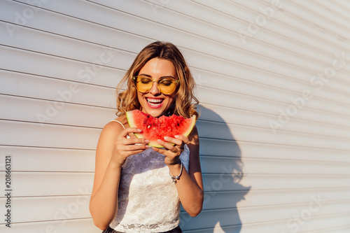 Pretty girl eating a watermelon, wearing yellow sunglasses, enjoying the summer days, outdoors.