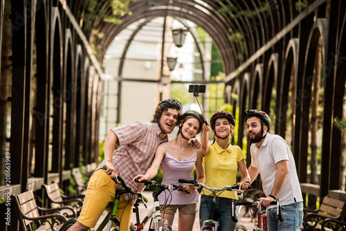 Happy students having fun outdoors. Group of happy cyclist taking picture using selfie stick outdoors. Summer rest concept.