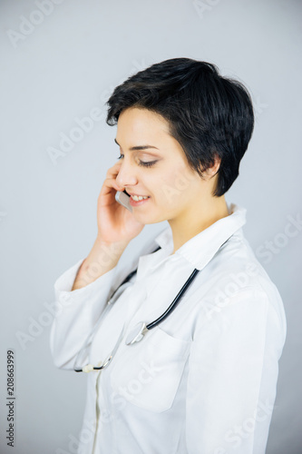 Friendly female doctor in lab coat with stethoscope talking with phone.