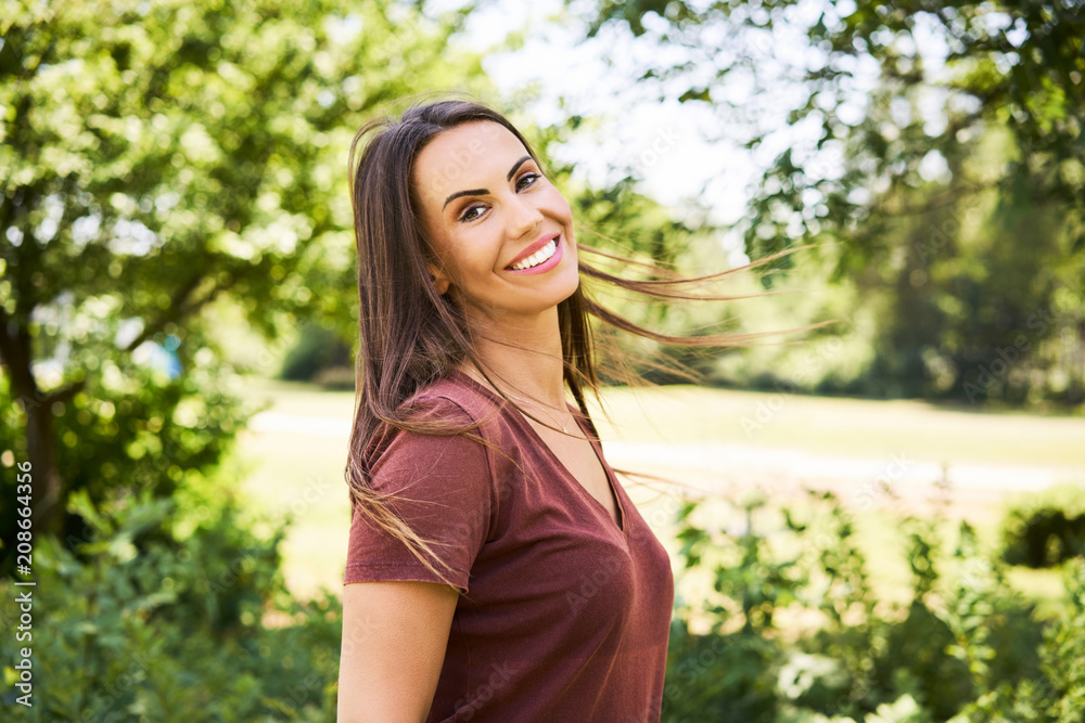 Portrait of young woman looking at camera and smiling while in park during summer Portrait of young woman looking at camera and smiling while in park during summer