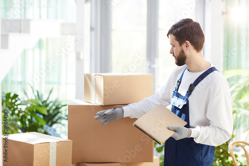 Foto Serious concentrated handsome young male mover in uniform analyzing package and