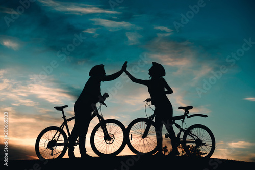 Man and woman giving five with hands outdoors. Couple of cyclists touching hand to hand on evening sky background. Unforgettable rest together.