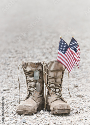 Old military combat boots with dog tags and two small American flags. Rocky gravel background with copy space. Memorial Day or Veterans day concept. Vintage tone.