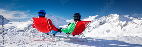 Young couple sitting on deck chairs and enjoying stunning view of Alps, Europe