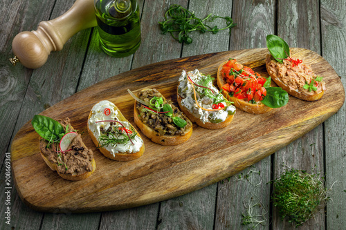 Classic Italian antipasti bruschetta set made of baguette tomato, meat pate, olives, cream cheese and tuna salad on a rustic wooden board. Top view.
