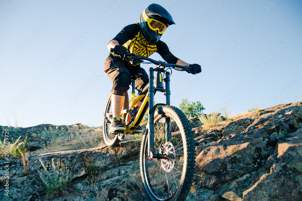 Naklejka premium Cyclist Riding the Mountain Bike on the Summer Rocky Trail at the Evening. Extreme Sport and Enduro Cycling Concept.