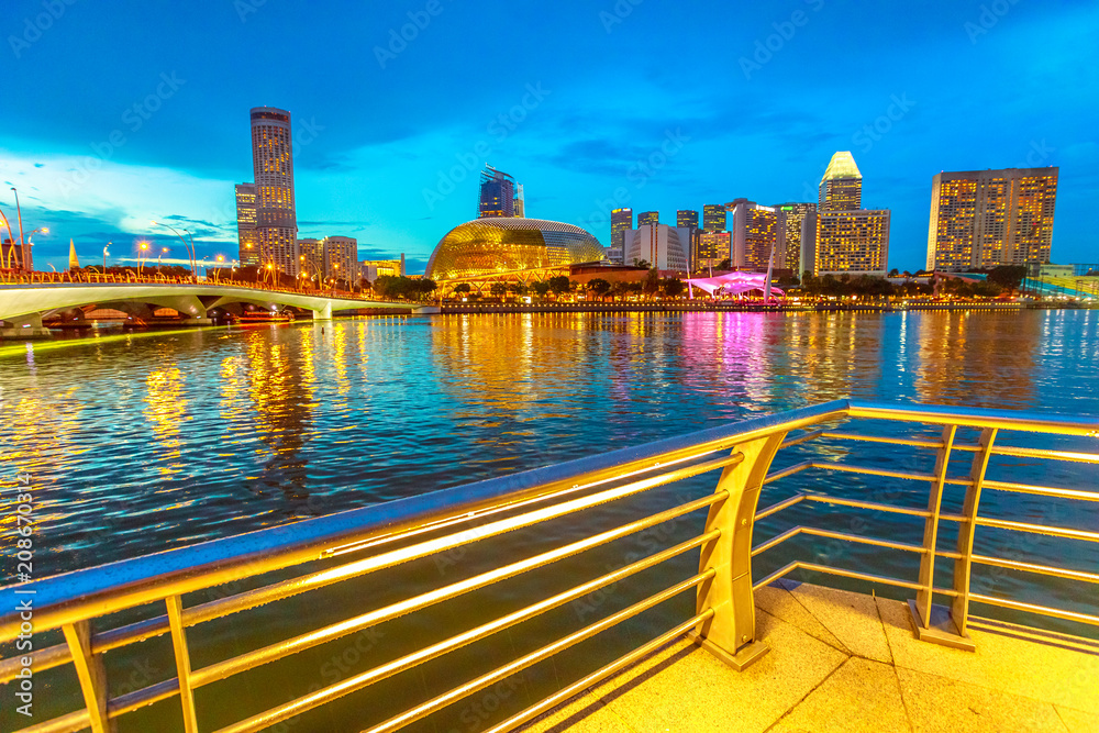 Obraz premium Panoramę zatoki mariny z mostem z wieczornymi światłami odbijającymi się w morzu o niebieskiej godzinie. Singapur gród w nocy. Nocna scena nadmorskiej promenady.