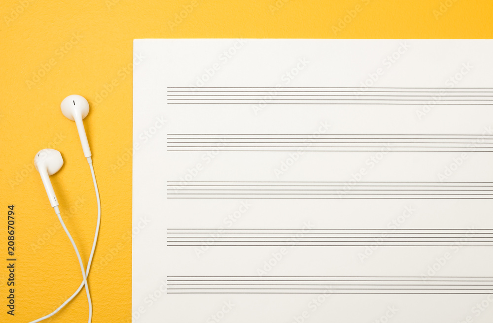 Fototapeta premium Earphones and blank music sheet on yellow background
