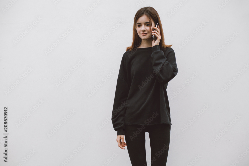 Young hipster smiling girl wearing blank black hoodie and jeans and talking  via mobile phone, mock-up of blank black sweatshirt, white background Stock  Photo | Adobe Stock