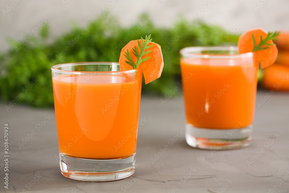 Two glasses of fresh carrot juice on grey concrete background