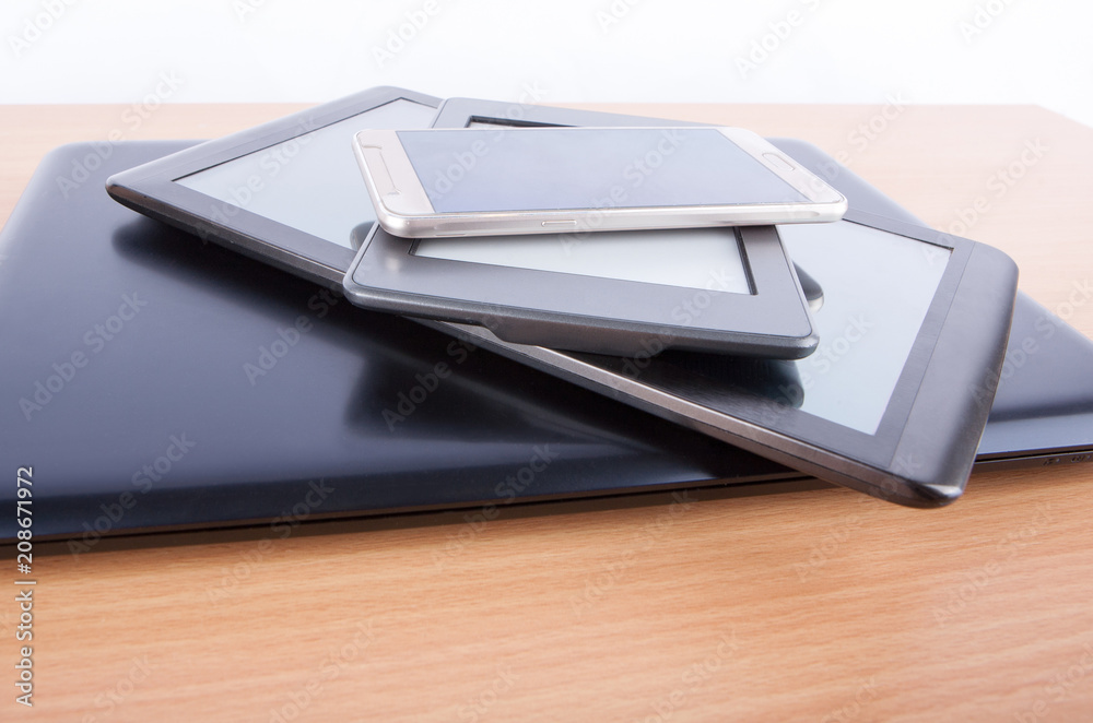 Stack of gadgets on an office desk - notebook, tablets, an ebook reader and a smatphone Stack of gadgets on an office desk - notebook, tablets, an ebook reader and a smatphone