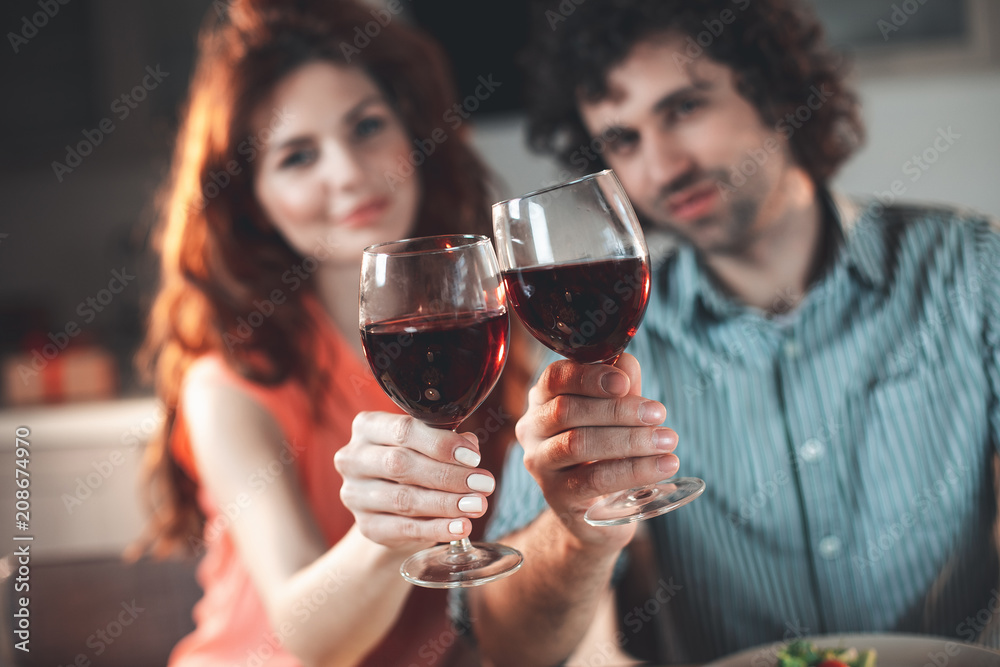 Cheers. Happy loving couple clinking glasses of wine while sitting in kitchen. Focus on red wine Cheers. Happy loving couple clinking glasses of wine while sitting in kitchen. Focus on red wine