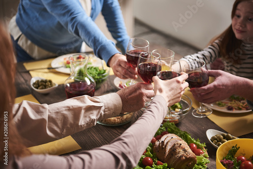 Close up of wine glasses holding by household members. They are sharing traditional wholesome dinner and spending time together