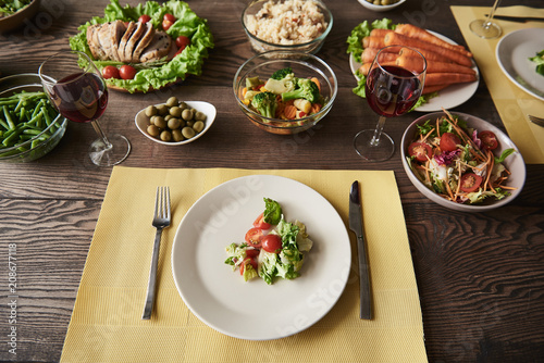 Fototapeta Naklejka Na Ścianę i Meble -  Top view of big brown table with white plates and bowls of healthy food. There are carrot, asparagus, tomatoes, lettuce, broccoli, olives, whole grain bread, baked meat and rice