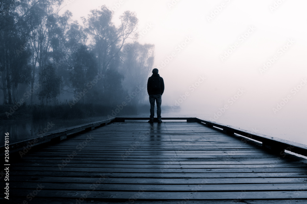 Person Standing at a Lake Boardwalk in Fog