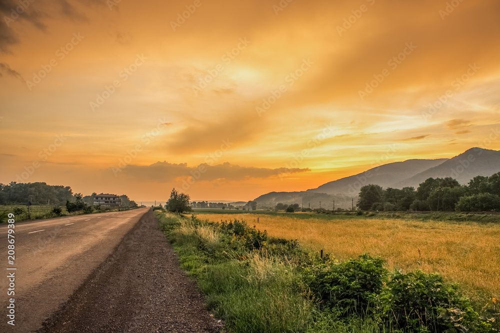 Fototapeta premium orange sunset evening country side landscape with lonely road concep