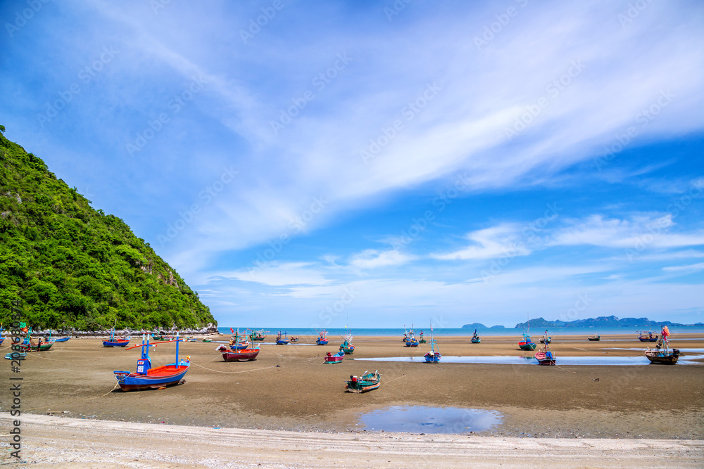 Many small fishing boats on sand beach during low tide with cloudy blue sky at Pranburi Prachuap-Kirikhan Thailand