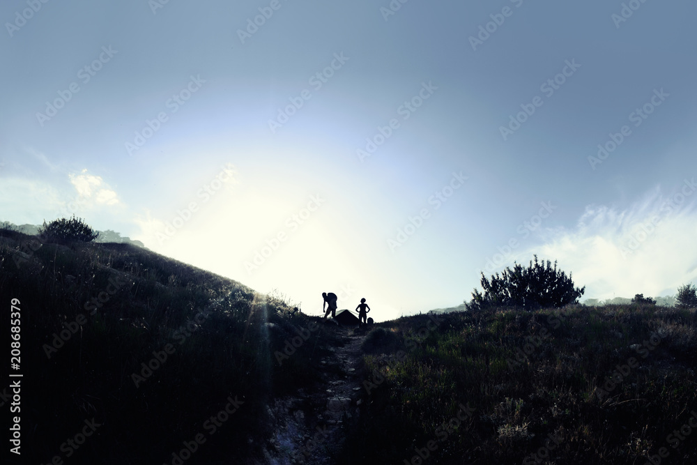 Photo of a black nature landscape photo with travelling people sillouettes and shining light on horizon.
