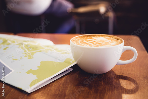 White coffee cup with latte art with travel map on brown wood table,Leisure activity.