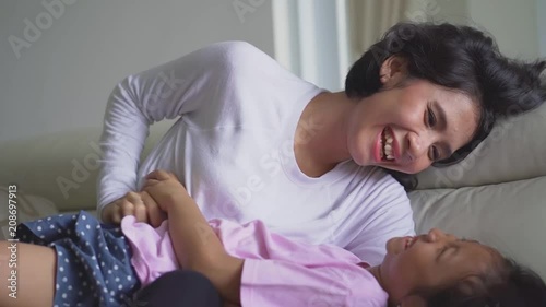 Cheerful little girl joking with her mother on the sofa in the living room at home