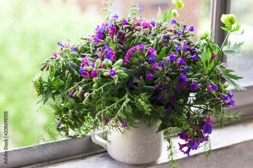 Wild forest meadow bouquet of cherry  lungwort  wild herbs in ceramic cup on window sill