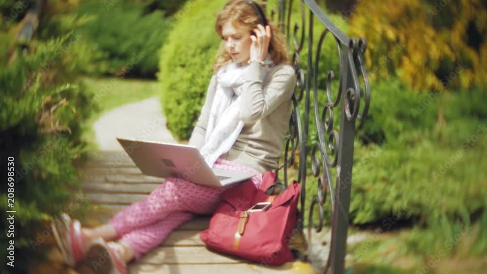 Woman with laptop relaxes on a bench in a beautiful green park. A young perennial woman in an arboretum working behind a laptop. Technology in the open air Woman with laptop relaxes on a bench in a beautiful green park. A young perennial woman in an arboretum working behind a laptop. Technology in the open air