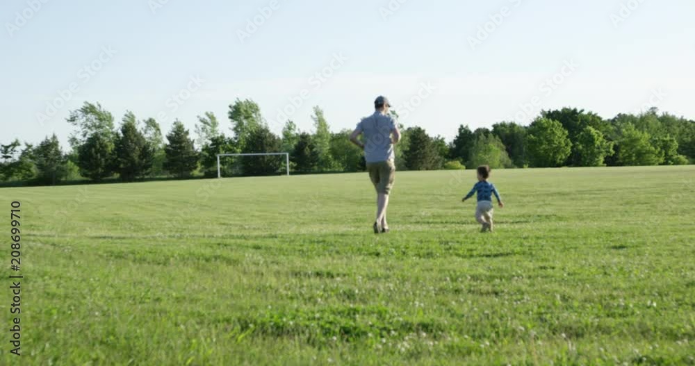 Toddler boy and father running on grassy field in summer - wide shot - rack focus Toddler boy and father running on grassy field in summer - wide shot - rack focus