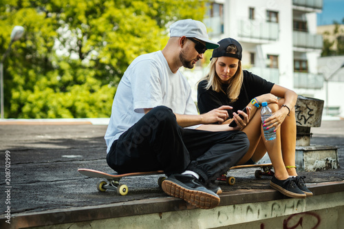 boy and girl on a skateboard are sitting and watching something on the mobile phone on a summer day
