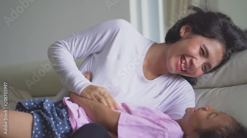 Happy young mother joking with her daughter while sitting on the sofa in the living room at home