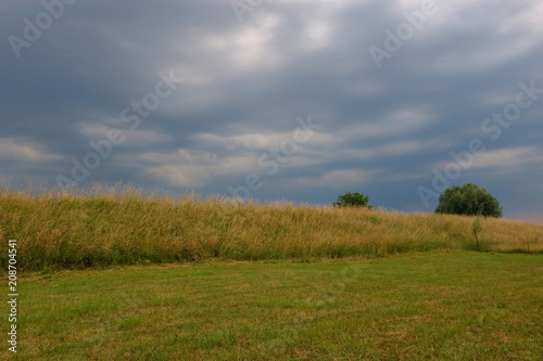 Ciemne, ciężkie, zachmurzone niebo nad płaskim krajobrazem, niedysoka skarpa porośnięta trawą, 
