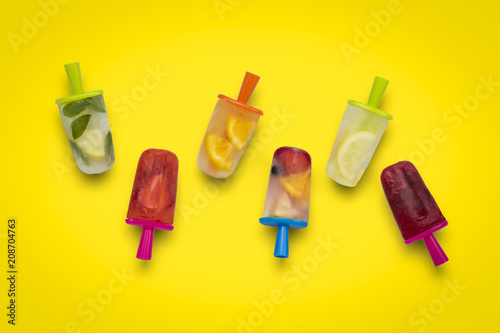 Homemade fruit popsicle on a yellow background. Strawberry, Lemon, Lemon with mint, Orange, Cherry, Multifruit. Flat lay, top view