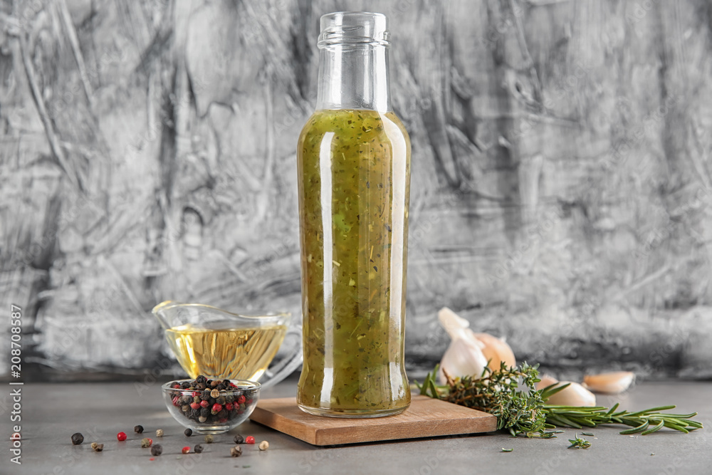 Bottle with tasty green sauce and herbs on table Bottle with tasty green sauce and herbs on table