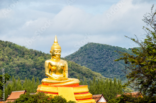 Big statue of Buddha in Thailand in front of mountain with blue sky.