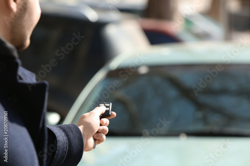 Man pushing button on remote control of car alarm system, outdoors