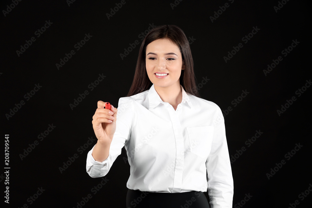 Young businesswoman writing on virtual screen against black background Young businesswoman writing on virtual screen against black background