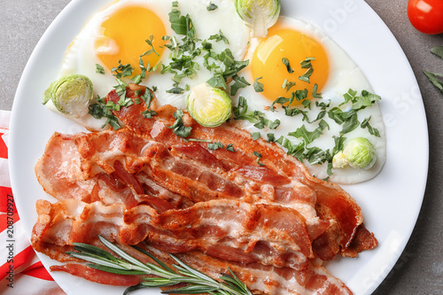 Plate with tasty bacon and fried eggs on table