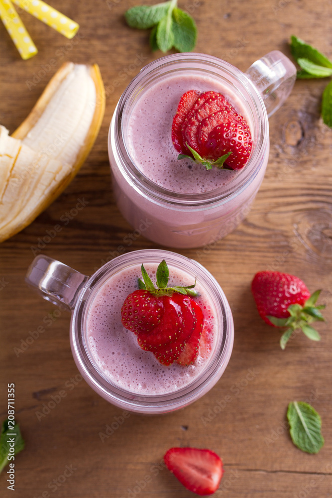 Two glasses of pink strawberry milkshake or cocktail. Strawberry banana smoothie on wooden table. overhead, vertical Two glasses of pink strawberry milkshake or cocktail. Strawberry banana smoothie on wooden table. overhead, vertical