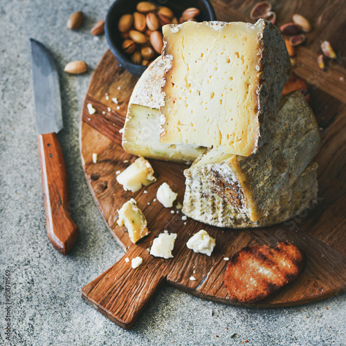 Cheese platter with cheese assortment, nuts, honey and bread on rustic wooden board over grey concrete background, selective focus, square crop. Party or gathering eating concept