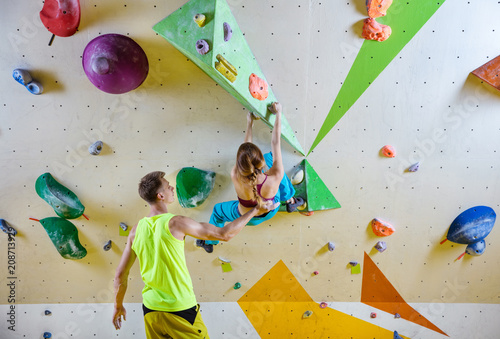 Young woman climbing bouldering problem (route), male instructor securing her