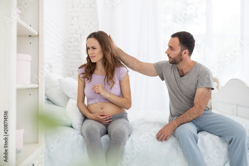 Dont worry. Appealing man and pregnant woman sitting on bed and man touching her head