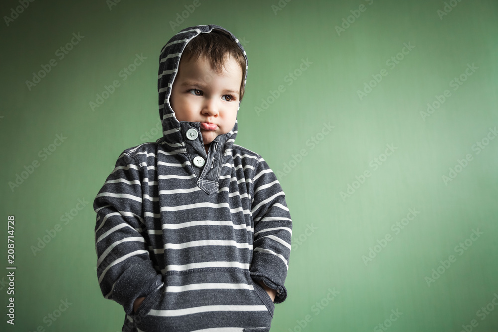 Gloomy cute little boy holding hands in pullover pockets.Free space for advertisement Gloomy cute little boy holding hands in pullover pockets.Free space for advertisement