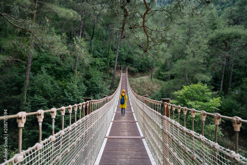 Fototapeta Naklejka Na Ścianę i Meble -  Woman with raincoat walikng on suspension bridge