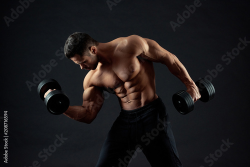Horizontal shot of muscular man lifting heavy dumbbells in gym. Having sexy athletic figure, strong body with clear muscles relief.Sport lifestyle. Regular gym trainings. Fit sporty body. Lifestyle. © serhiibobyk