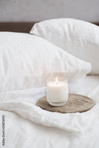 Burning candle on wooden tray on white natural linen