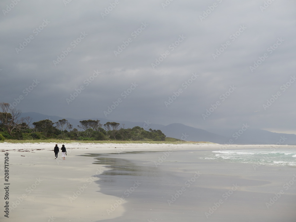 Pastell colored dramatic sky with two people walking at Bicheno Beach, Bay of Fires, Tasmania, Australia