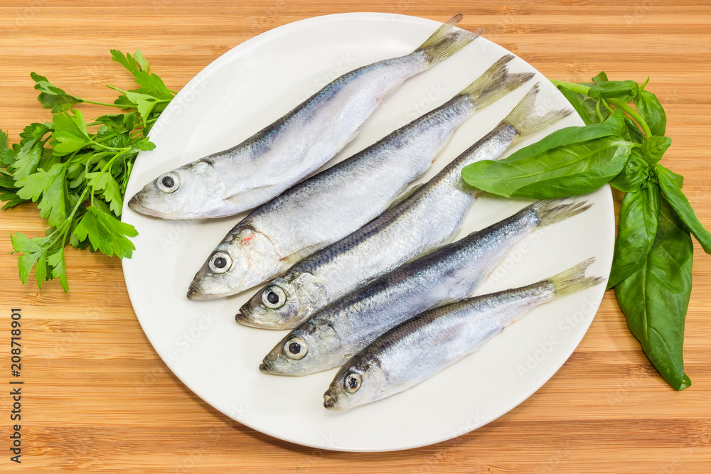 Defrosted baltic herring on the white dish and greens closeup Defrosted baltic herring on the white dish and greens closeup
