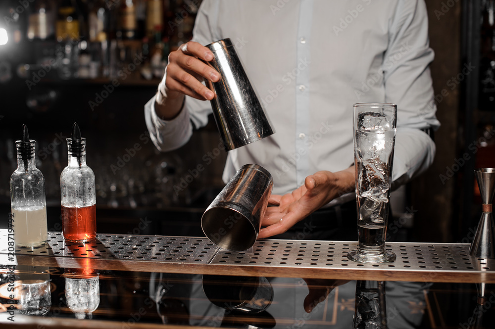Bartender holding a steel cocktail shaker at the bar counter