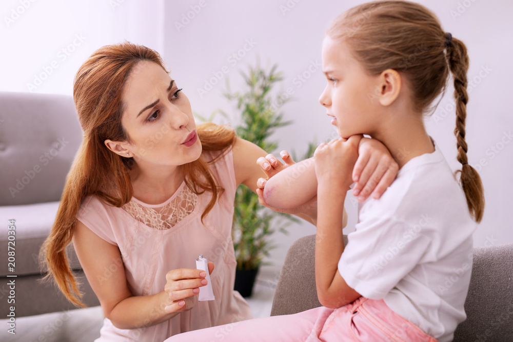 Everything will be ok. Caring young woman trying to ease pain while proving first aid to her daughter Everything will be ok. Caring young woman trying to ease pain while proving first aid to her daughter